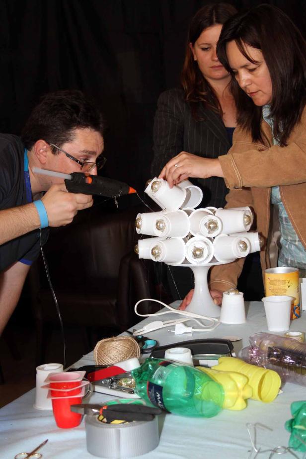 Drei Personen basteln eine Lampe aus Plastikbechern und einer Heißklebepistole.