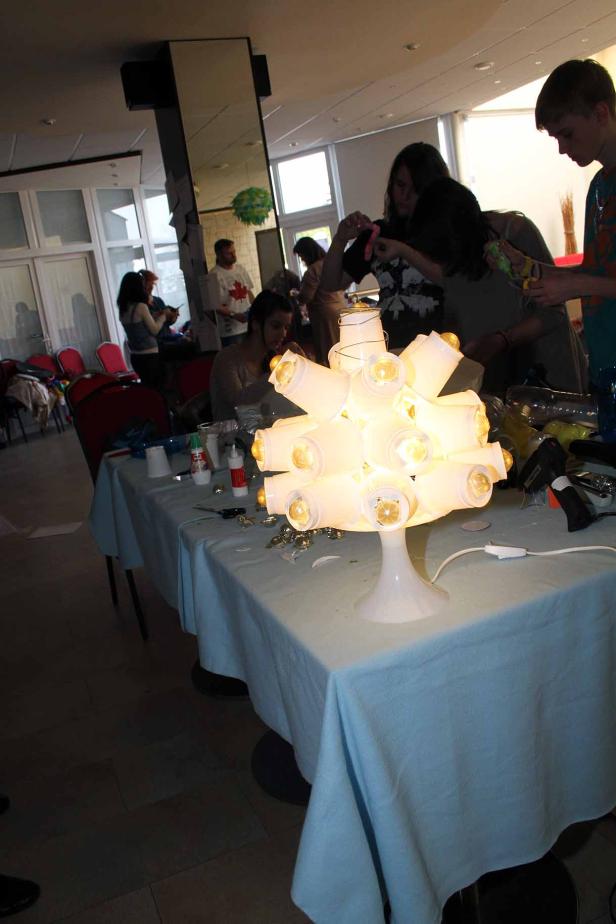 Menschen basteln an einem Tisch mit einer Lampe aus Plastikbechern.