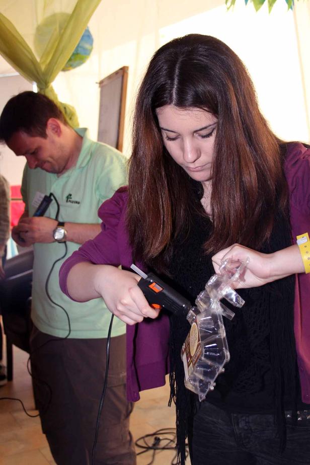 Eine Frau benutzt eine Heißklebepistole, während ein Mann im Hintergrund ebenfalls bastelt.