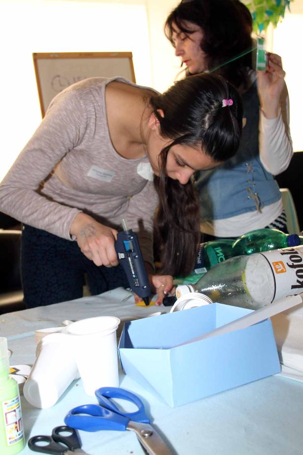 Eine Frau klebt mit einer Heißklebepistole etwas an einem Basteltisch.