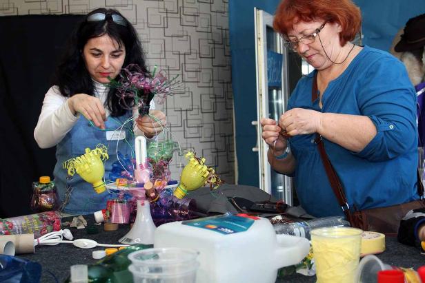 Zwei Frauen basteln mit wiederverwerteten Plastikflaschen an einem Tisch.