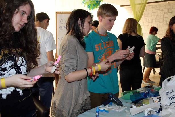 Eine Gruppe junger Leute bastelt mit Klebstoff, Schere und bunten Materialien an einem Tisch.