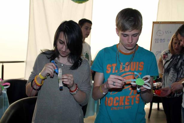 Zwei Jugendliche basteln mit Papier und Klebstoff an einem Tisch.