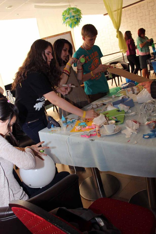 Eine Gruppe von Jugendlichen bastelt an einem Tisch mit verschiedenen Materialien.