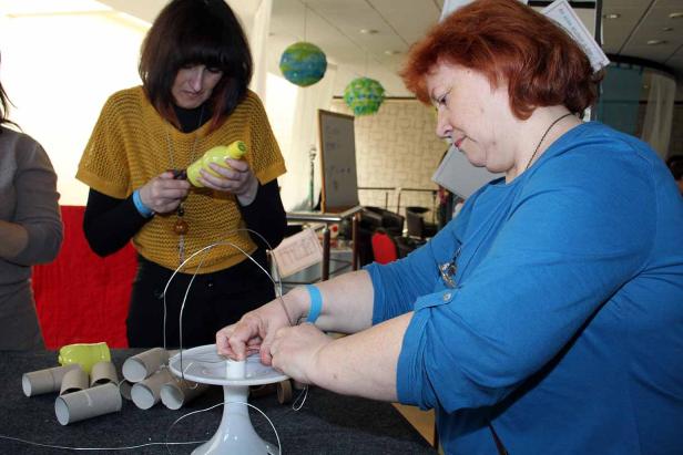 Zwei Frauen basteln mit leeren Toilettenpapierrollen und Draht an einem Tisch.
