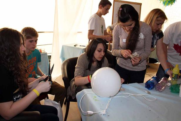 Eine Gruppe von Jugendlichen bastelt an einem Tisch mit verschiedenen Materialien.