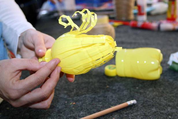 Jemand bastelt eine gelbe Blume aus einer Plastikflasche.