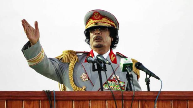 Muammar al-Gaddafi in Uniform gestikuliert vor Mikrofonen.