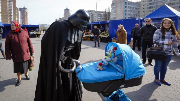 Eine als Darth Vader verkleidete Person schiebt einen Kinderwagen auf einem Markt.