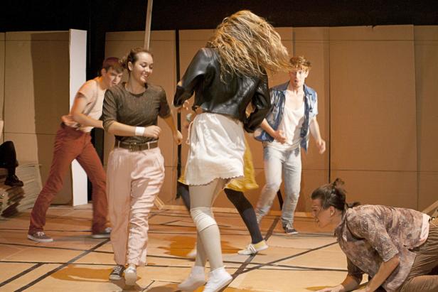 Mehrere Personen tanzen auf einer Bühne vor einem braunen Hintergrund.