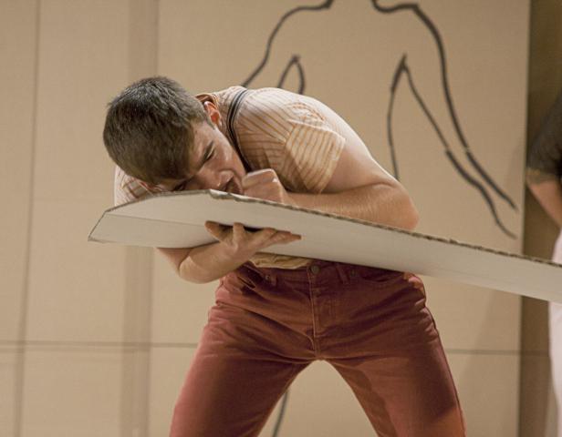 Ein Mann in roter Hose beißt in eine Pappe vor einer Wandzeichnung.