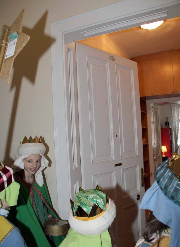 Kinder, als die Heiligen Drei Könige verkleidet, stehen vor einer Tür.