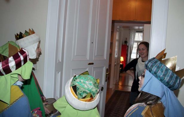 Sternsinger stehen vor einer Tür, während eine Frau im Hintergrund zusieht.