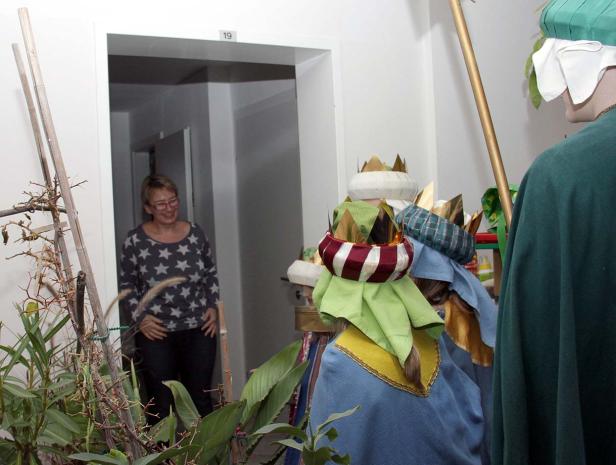 Eine Frau steht in einer Tür, während drei Figuren mit Kronen im Raum stehen.