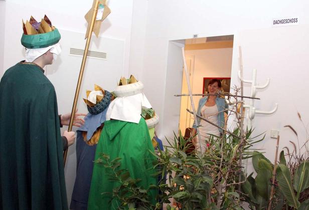 Sternsinger ziehen durch ein Haus, eine Frau steht im Hintergrund in einer Tür.