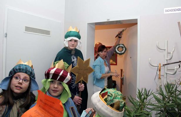 Eine Gruppe Kinder, verkleidet als Sternsinger, steht vor einer Tür.