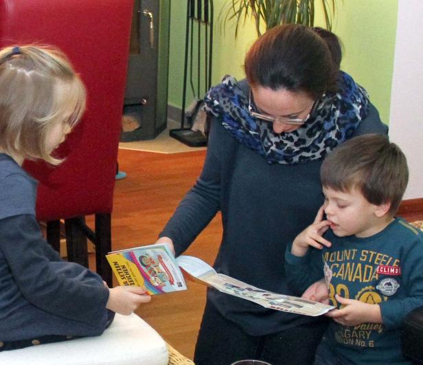 Eine Frau liest mit zwei Kindern ein Buch.