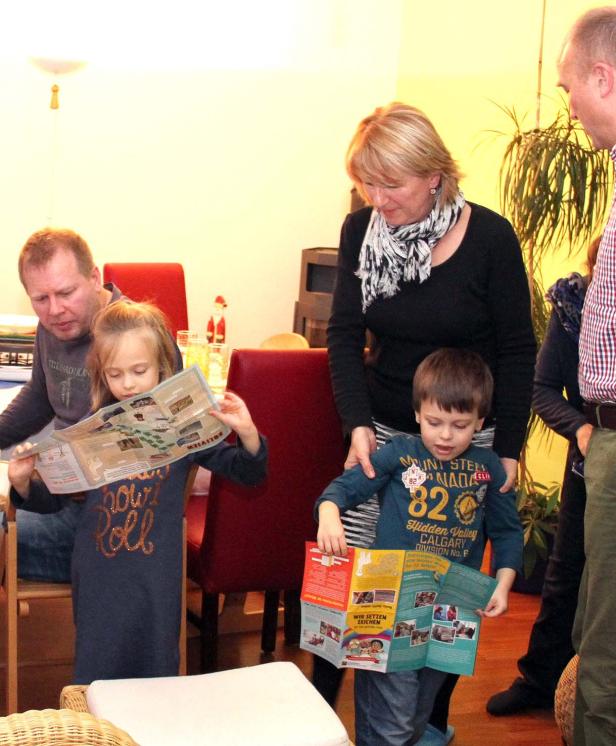 Eine Familie betrachtet gemeinsam Karten und Broschüren in einem Wohnzimmer.