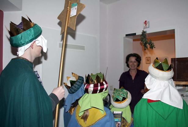 Eine Gruppe Sternsinger mit ihren Kronen und Gewändern besucht eine Frau.