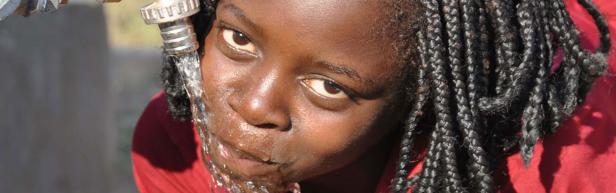 Ein junges Mädchen trinkt Wasser aus einem Wasserhahn.