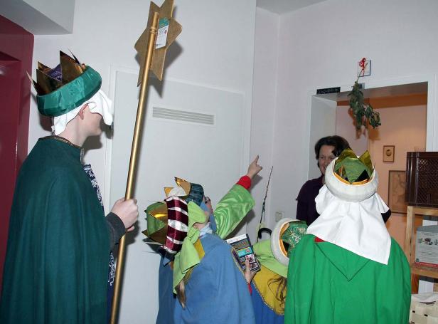Eine Gruppe Sternsinger in bunten Kostümen besucht ein Haus.