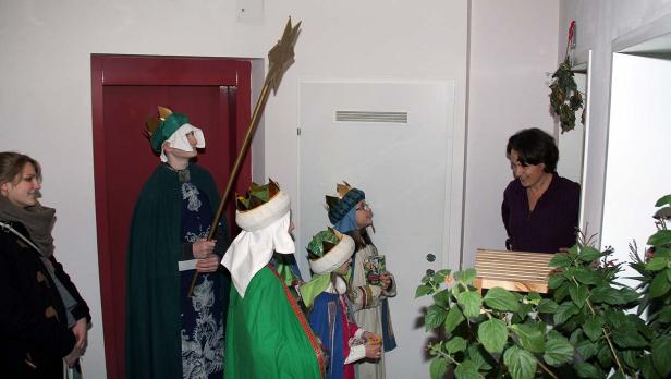Sternsinger besuchen ein Haus und werden von einer Frau empfangen.
