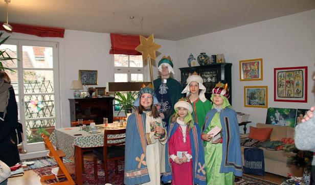 Eine Gruppe Kinder, als Sternsinger verkleidet, steht in einem Wohnzimmer.