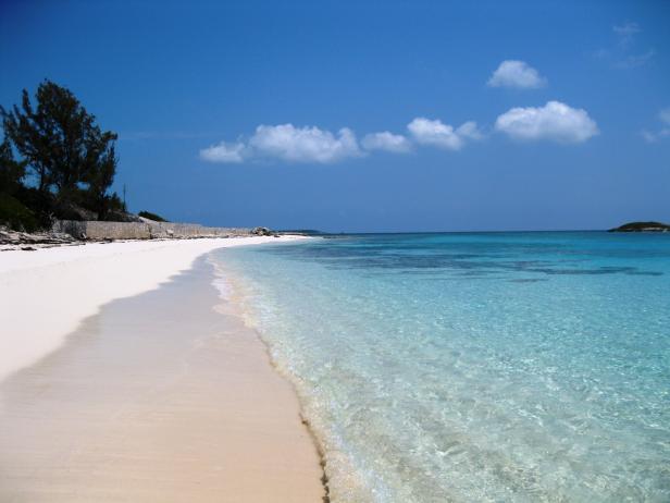 Ein ruhiger Strand mit weißem Sand und türkisfarbenem Wasser unter blauem Himmel.
