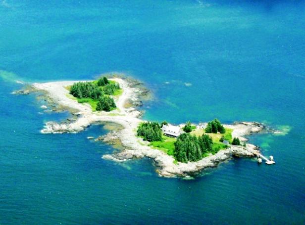 Luftaufnahme einer kleinen Insel mit einem Haus und einigen Bäumen im blauen Meer.