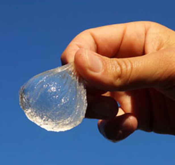 Eine Hand hält ein durchsichtiges, gallertartiges Objekt vor blauem Himmel.