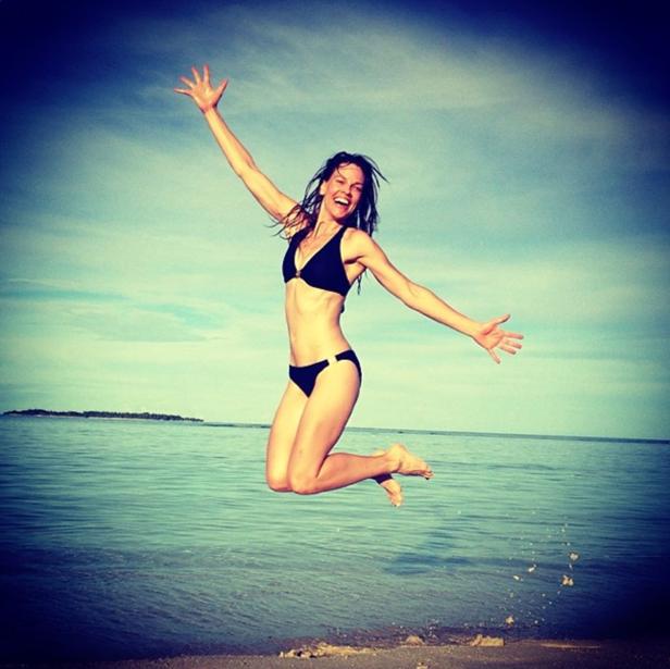 Eine Frau springt am Strand in einem schwarzen Bikini in die Luft.