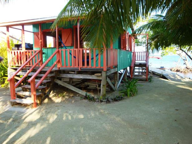 Ein farbenfrohes Strandhaus auf Stelzen mit einer Veranda und Blick auf das Meer.