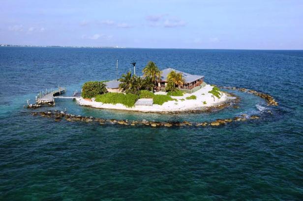 Eine kleine Insel mit einem Haus, Palmen und einem Steg im türkisfarbenen Meer.
