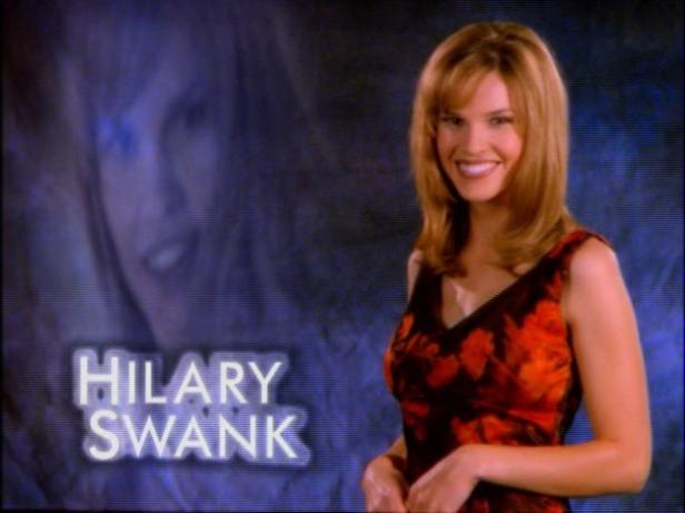 Ein Porträt der lächelnden Schauspielerin Hilary Swank vor einem blauen Hintergrund.