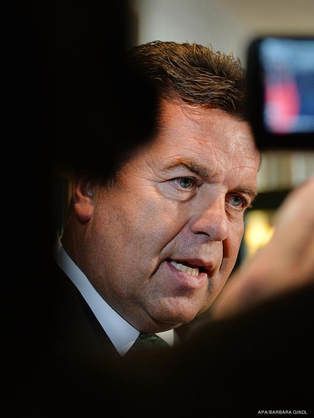 Ein Mann im Anzug spricht vor einer unscharfen Menschenmenge.