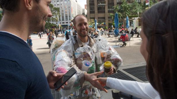 Ein Mann in einer Jacke aus Müll gibt einer Frau einen Kaffee.