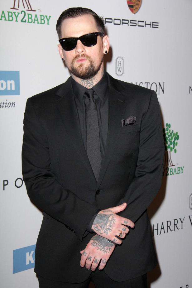 Ein Mann mit Tattoos und Sonnenbrille in einem schwarzen Anzug.