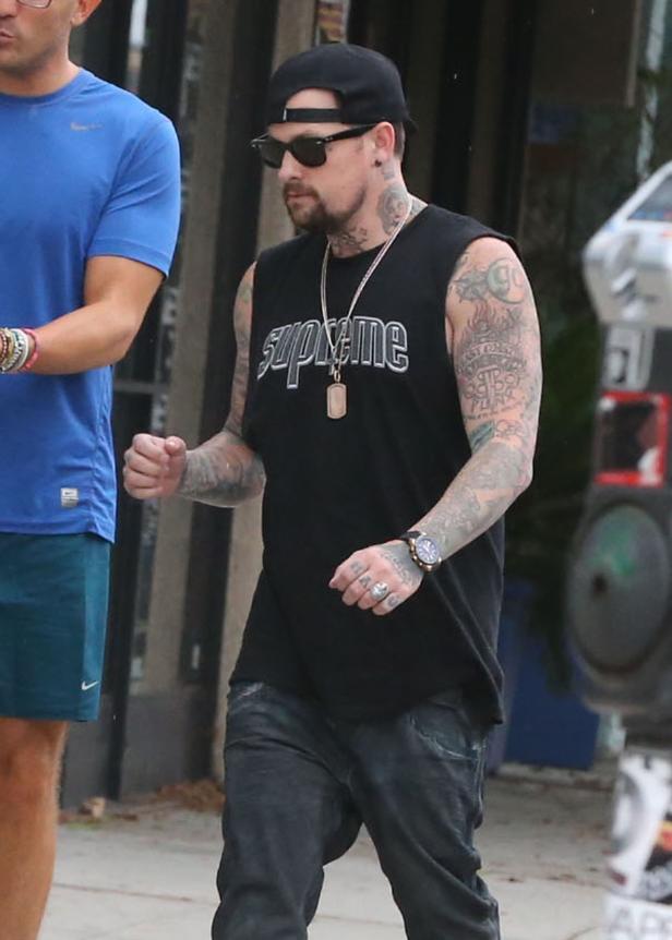 Ein tätowierter Mann mit Kappe und Sonnenbrille trägt ein schwarzes Supreme-Shirt.