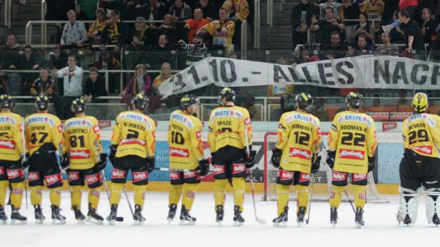 Eishockeyspieler in gelb-schwarzen Trikots stehen auf dem Eis vor einem Transparent mit der Aufschrift „31.10. – ALLES NACH“.