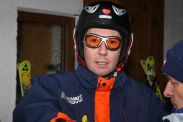 Ein Mann mit Skibrille und Helm steht vor einem Paar Skiern.