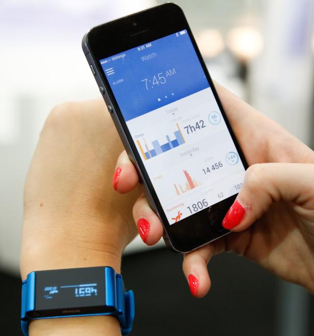 Eine Frau betrachtet ihre Gesundheitsdaten auf einem Smartphone und einem blauen Fitness-Tracker.