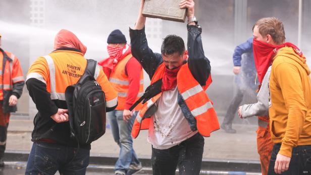 Ein Demonstrant hält einen Stein über den Kopf, während er von Wasserwerfern bespritzt wird.