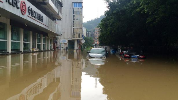 Überschwemmte Straße in China mit Autos, die im braunen Wasser stehen.