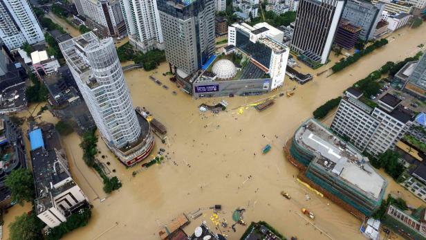 Luftaufnahme einer überfluteten Stadt mit Hochhäusern und braunem Wasser.