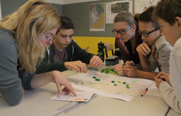 Eine Gruppe von Schülern plant mit einem Stadtplan und grünen Bausteinen eine Bebauung.
