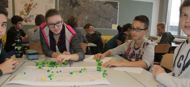 Schüler arbeiten mit einem Stadtplan und bunten Bauklötzen im Klassenzimmer.