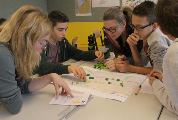 Eine Gruppe von Schülern plant mit Legosteinen auf einer Karte eine Stadt.