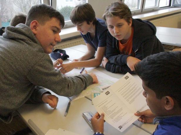 Eine Gruppe von Schülern arbeitet gemeinsam an einem Tisch an einer Aufgabe.