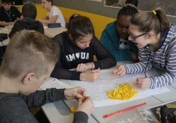 Eine Gruppe von Schülern arbeitet mit Legosteinen an einem Tisch mit einem Stadtplan.