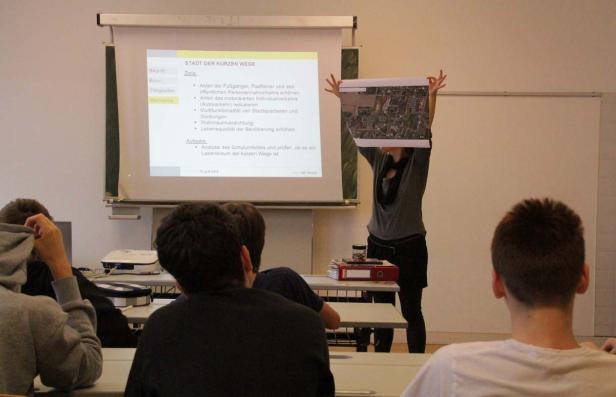 Eine Frau präsentiert eine Karte vor einer Klasse, während eine Präsentation läuft.